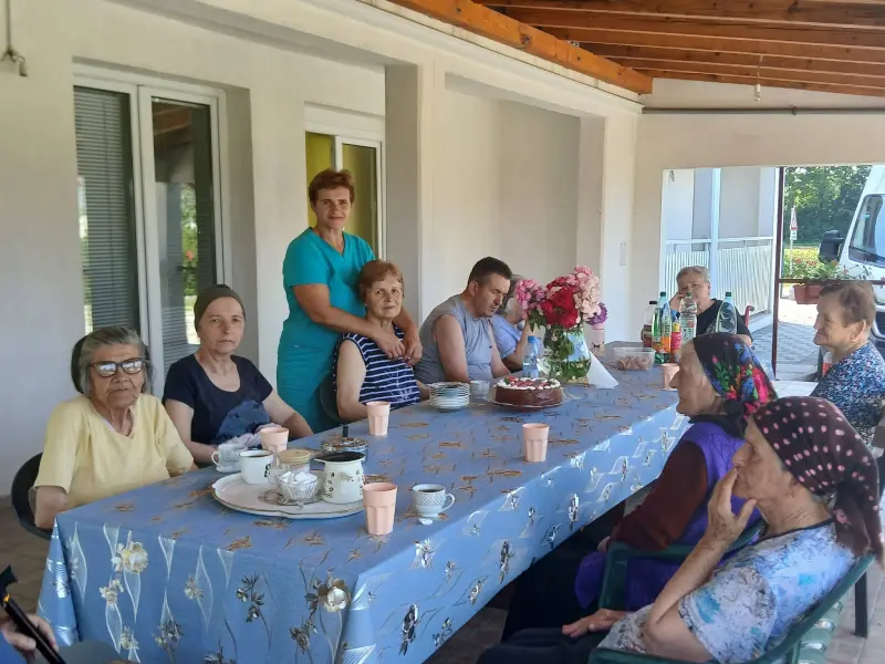 Korisnici i osoblje doma Oaza Mira okupljeni za stolom na natkrivenoj terasi