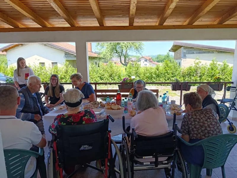 Korisnici i osoblje doma zajedno provode vrijeme za stolom na terasi